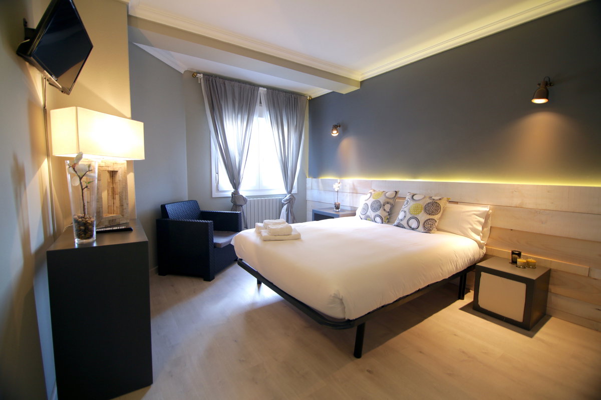 Habitación de hotel moderna con pared oscura iluminada, toallas dobladas sobre la cama y sillón de rejilla
