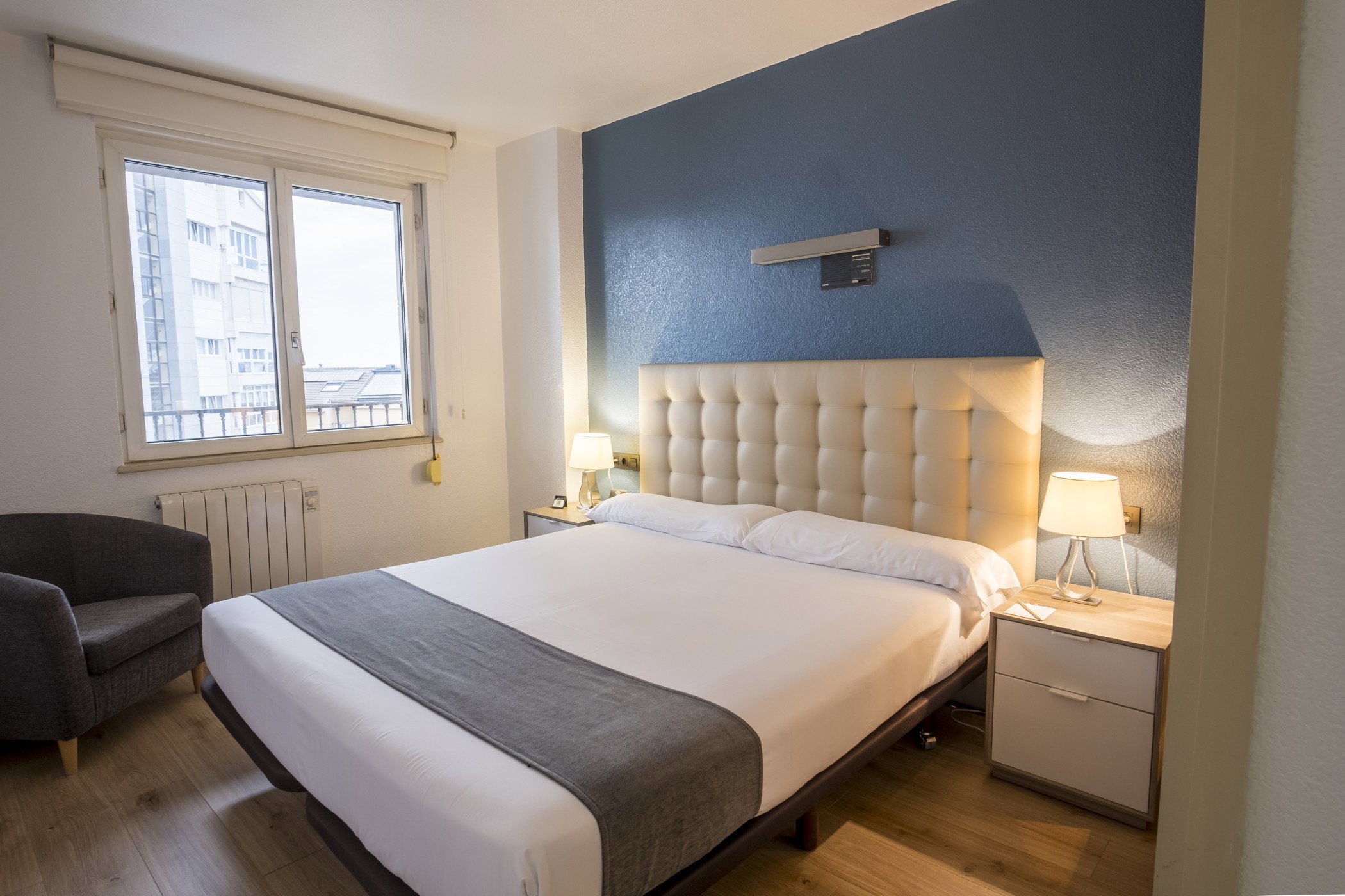 Habitación doble con cabecero acolchado beige, pared azul y mesitas de noche con lámparas