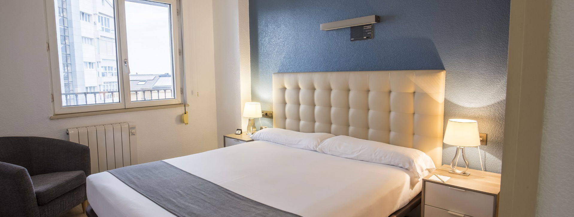 Habitación doble con cabecero acolchado beige, pared azul y mesitas de noche con lámparas