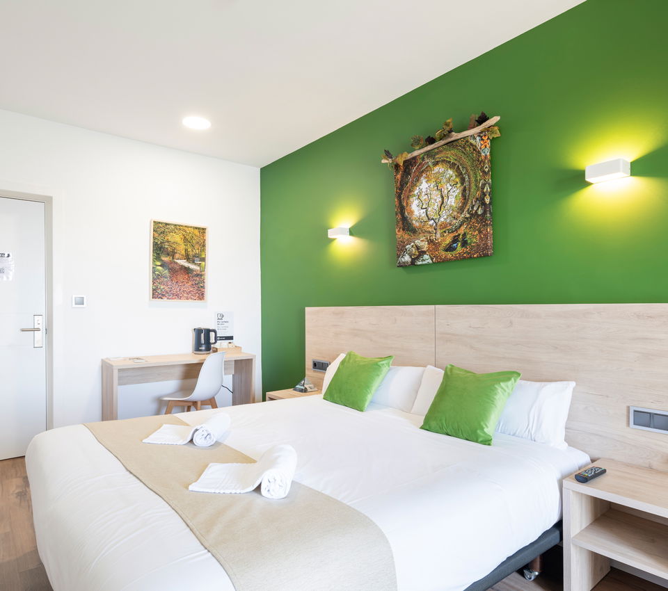 Habitación de hotel con pared verde, cabecero de madera, cojines verdes y escritorio