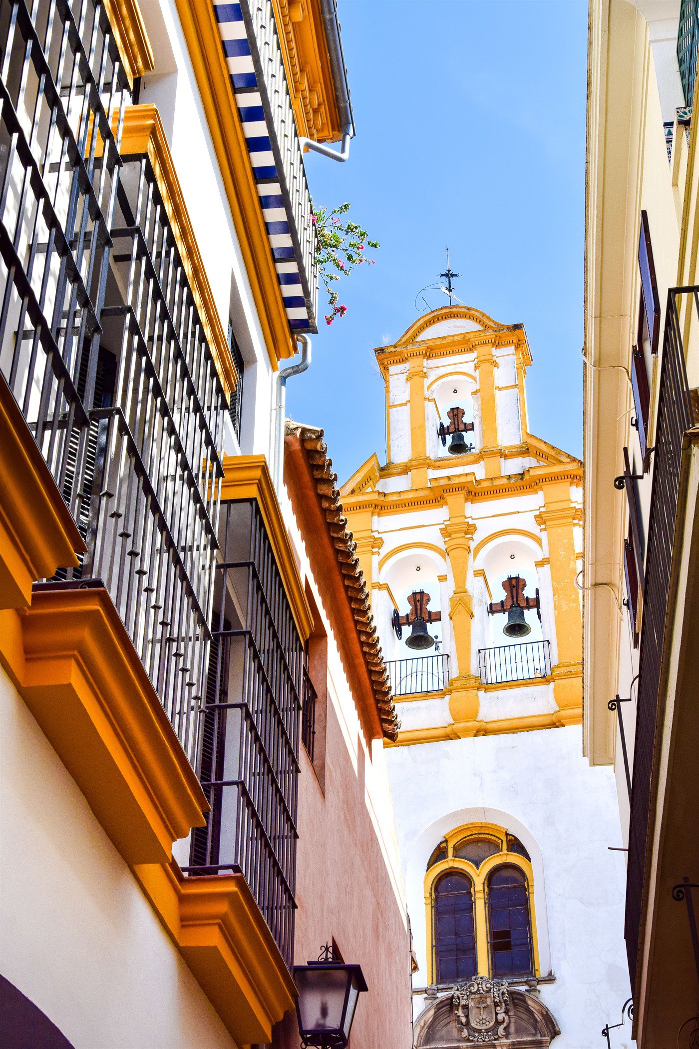 Callejuela del barrio de Santa Cruz con balcones enrejados y la torre-campanario de una iglesia asomando entre los tejados