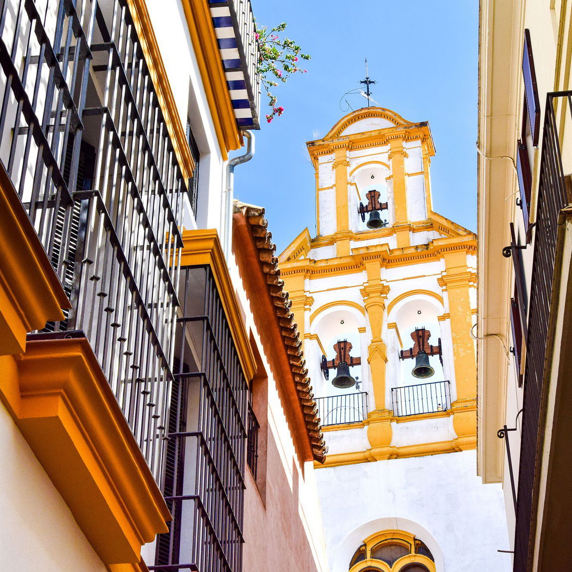 Callejuela del barrio de Santa Cruz con balcones enrejados y la torre-campanario de una iglesia asomando entre los tejados