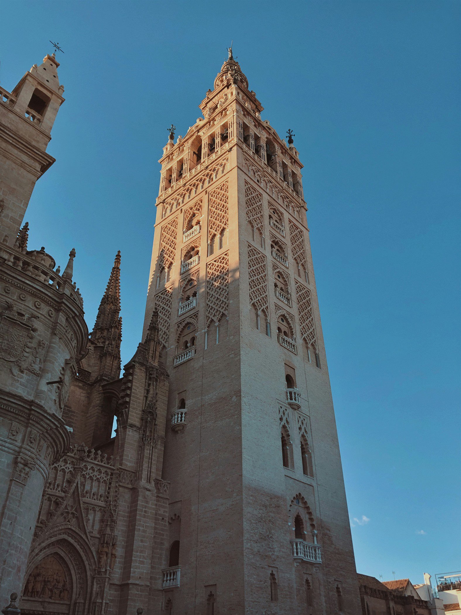 Vista de la Giralda, la torre campanario de la Catedral de Sevilla, con su remate renacentista y celosías de ladrillo bajo un cielo azul despejado