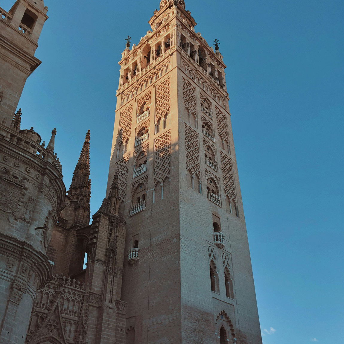 Vista de la Giralda, la torre campanario de la Catedral de Sevilla, con su remate renacentista y celosías de ladrillo bajo un cielo azul despejado