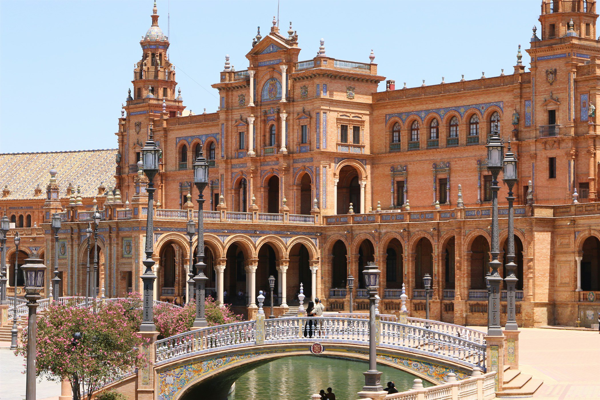 Fachada monumental de la Plaza de España de Sevilla con su torre central, arcos de ladrillo y el puente sobre el canal en primer plano