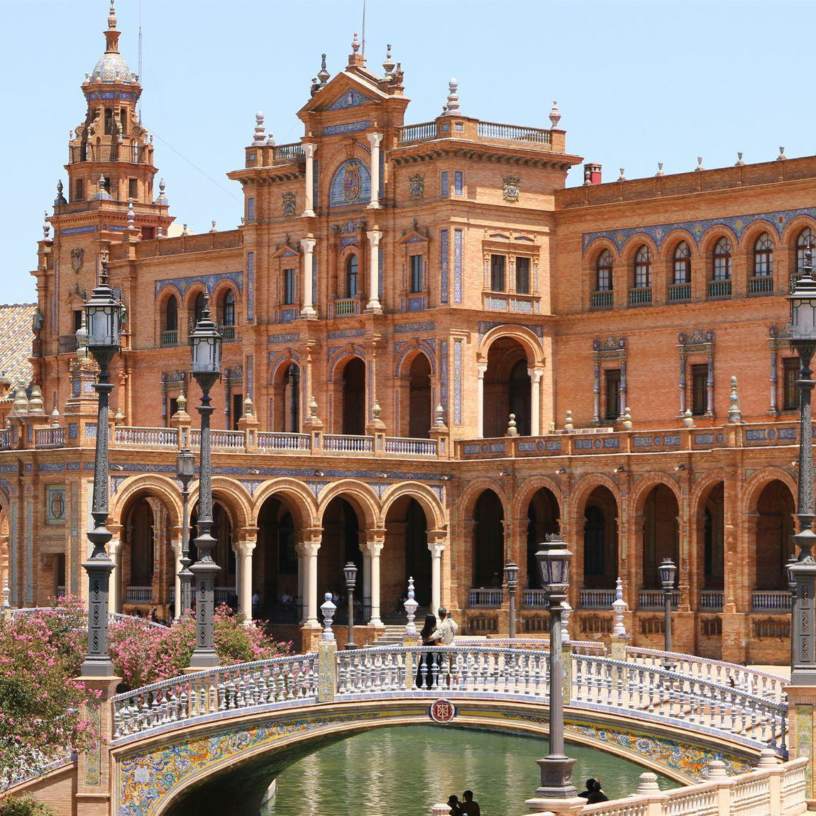 Fachada monumental de la Plaza de España de Sevilla con su torre central, arcos de ladrillo y el puente sobre el canal en primer plano