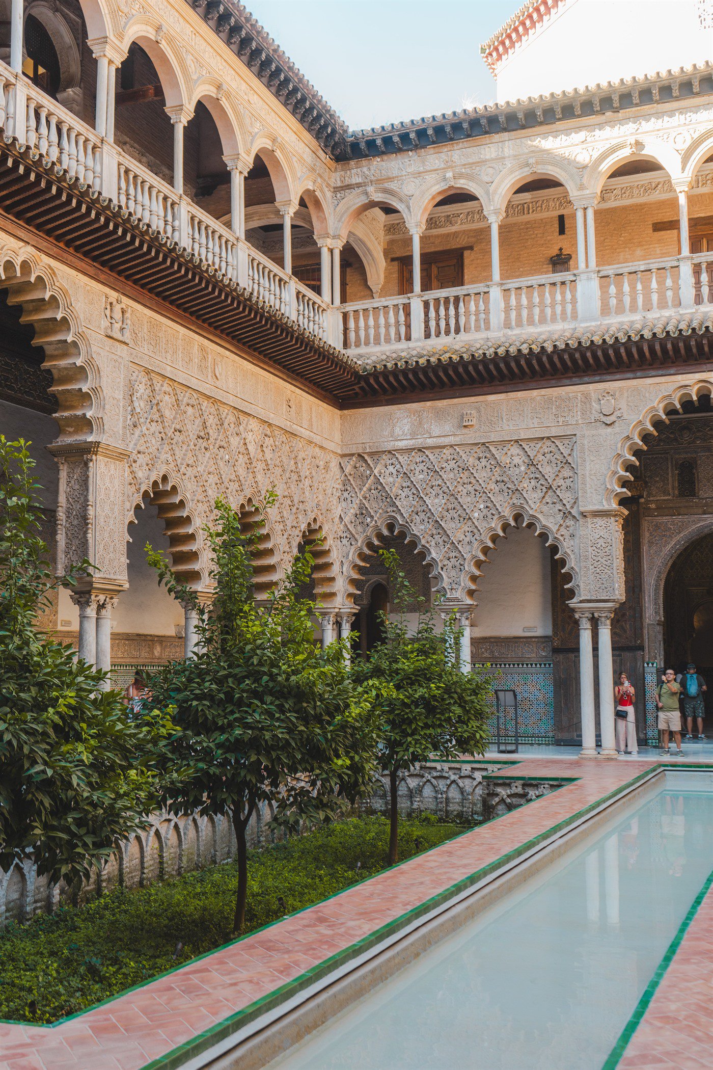 Patio de las Doncellas del Real Alcázar de Sevilla, con arcos mudéjares tallados, naranjos y una alberca de agua
