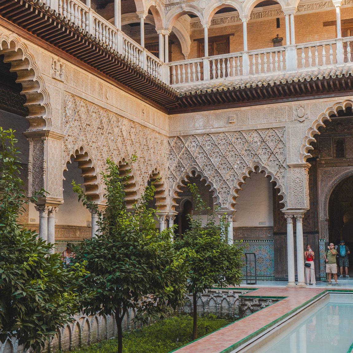 Patio de las Doncellas del Real Alcázar de Sevilla, con arcos mudéjares tallados, naranjos y una alberca de agua