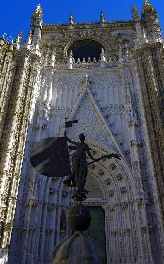 Estatua del Giraldillo con escudo y palma frente a la portada gótica de la Catedral de Sevilla