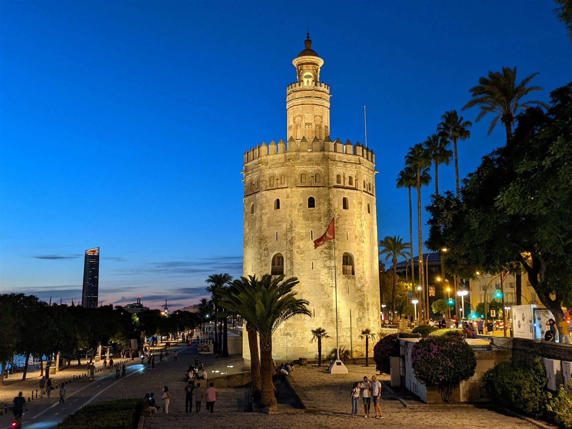 La Torre del Oro iluminada de noche junto al paseo del río Guadalquivir, con palmeras alrededor