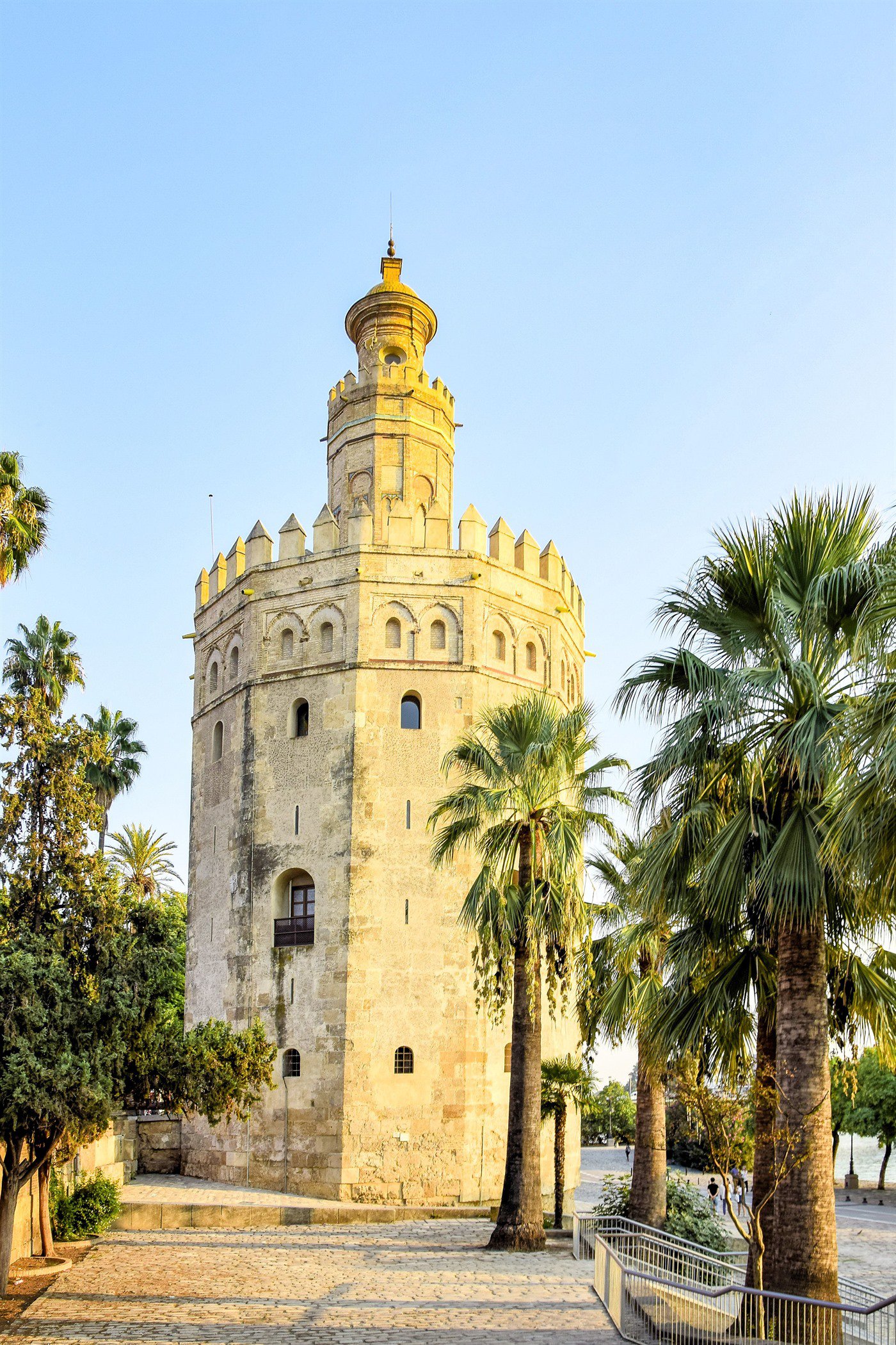 La Torre del Oro junto al río Guadalquivir, rodeada de palmeras, al atardecer