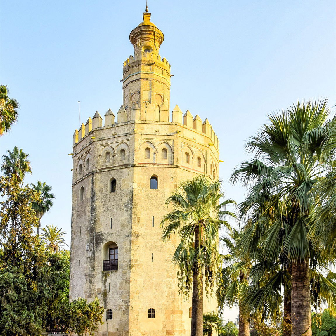 La Torre del Oro junto al río Guadalquivir, rodeada de palmeras, al atardecer