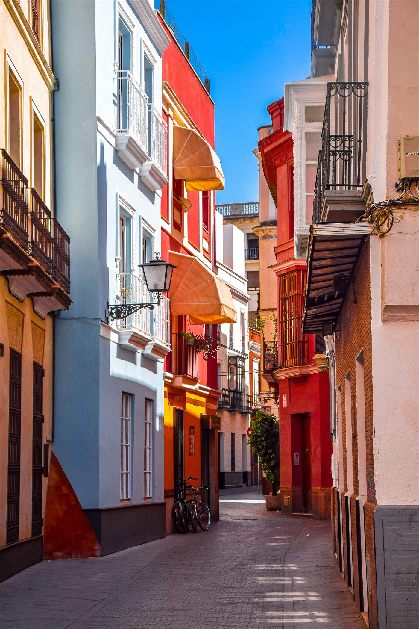 Calle estrecha del centro histórico de Sevilla con fachadas de colores, toldos y bicicletas aparcadas
