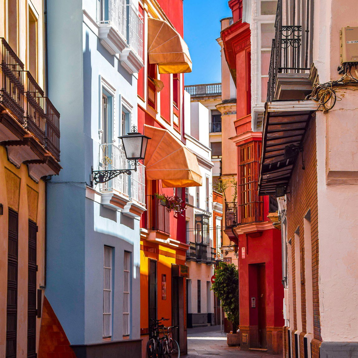 Calle estrecha del centro histórico de Sevilla con fachadas de colores, toldos y bicicletas aparcadas